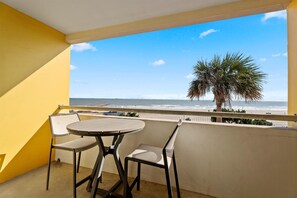 Enjoy breathtaking views of the beach from this balcony, featuring a round table and two chairs.