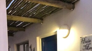 Ein schmaler Flur mit einer blauen Tür, einem kleinen Schild mit der Aufschrift 'Huis Man' und zwei Blumentöpfen.