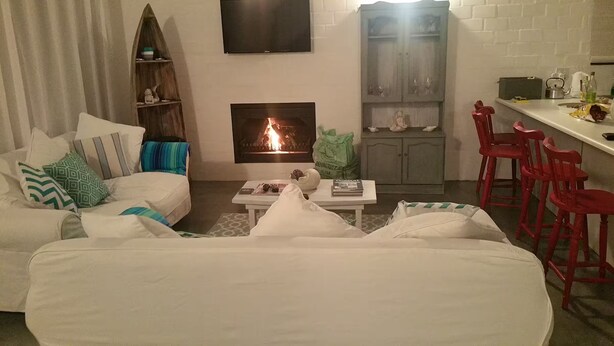 Ein Wohnzimmer mit Kamin, einem weißen Sofa, einem Couchtisch und einer Küchenzeile mit roten Stühlen.