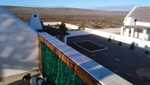 Eine Dachterrasse mit Blick auf eine karge Landschaft, ein kleiner Pool und ein weißes Gebäude mit grauem Dach.