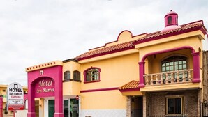 Un hôtel à la façade jaune et aux touches roses, doté d’une entrée imposante et d’une enseigne.