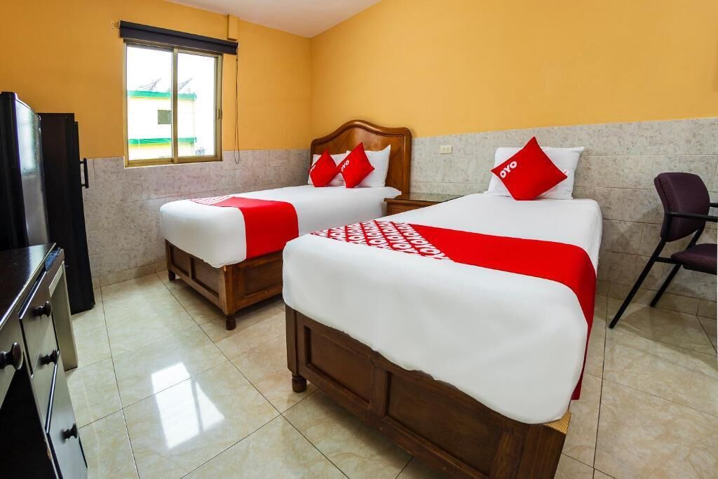 A hotel room with two beds, a window, a chair, and a TV.