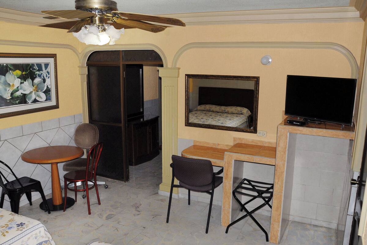 A compact room with a bed, a desk, a chair, a television, and a ceiling fan.