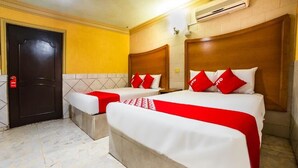 Une chambre d’hôtel avec deux lits, chacun recouvert d’une couvre-lit rouge et blanche et agrémenté d’oreillers assortis. On y trouve une porte avec une poignée rouge, un sol carrelé et une tête de lit en bois.