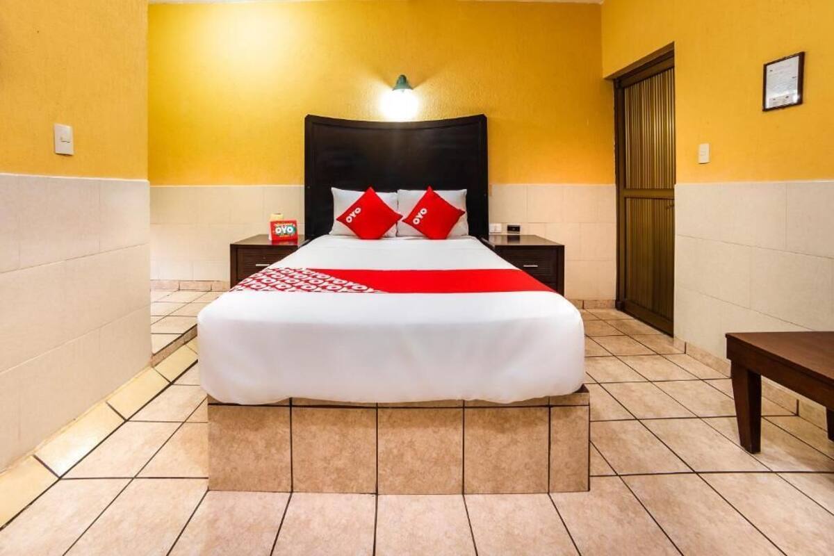 A hotel room with a bed, a nightstand, a wooden bench, and a door.