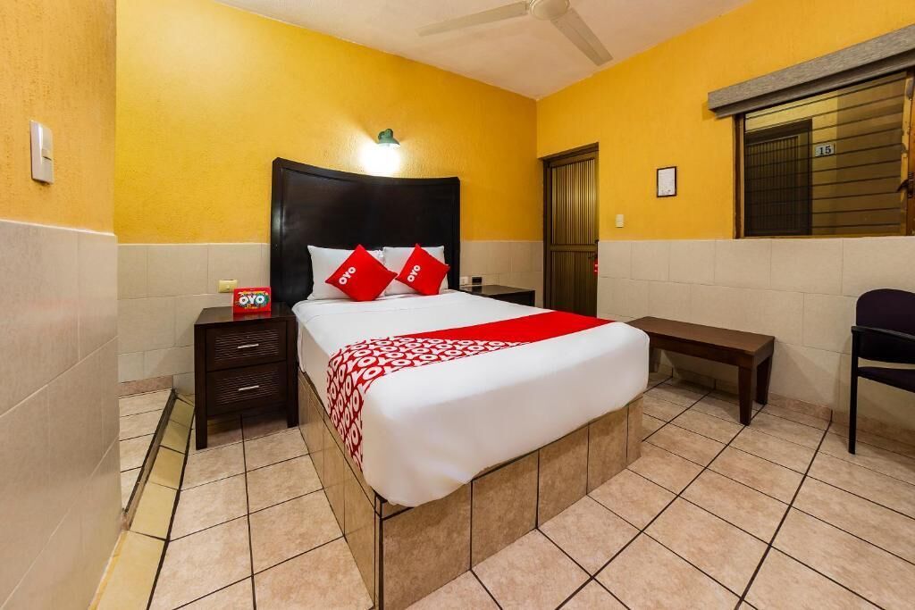 Una habitación de hotel con cama, mesita de noche, banco y puerta.