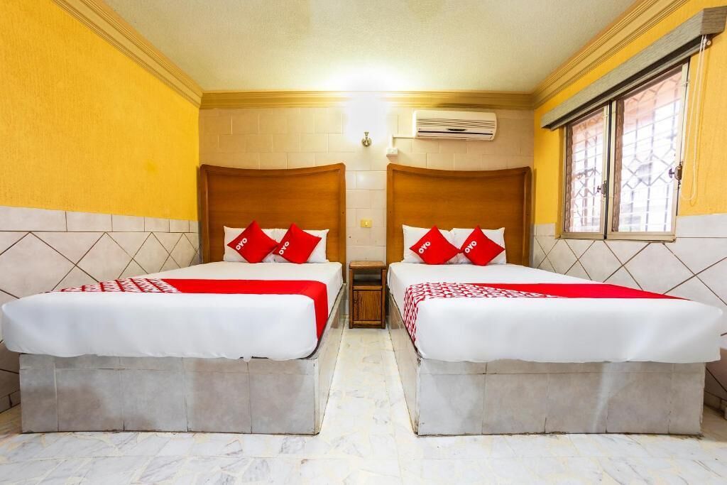 Habitación de hotel con dos camas, cada una con cabecero de madera y almohadas rojas.