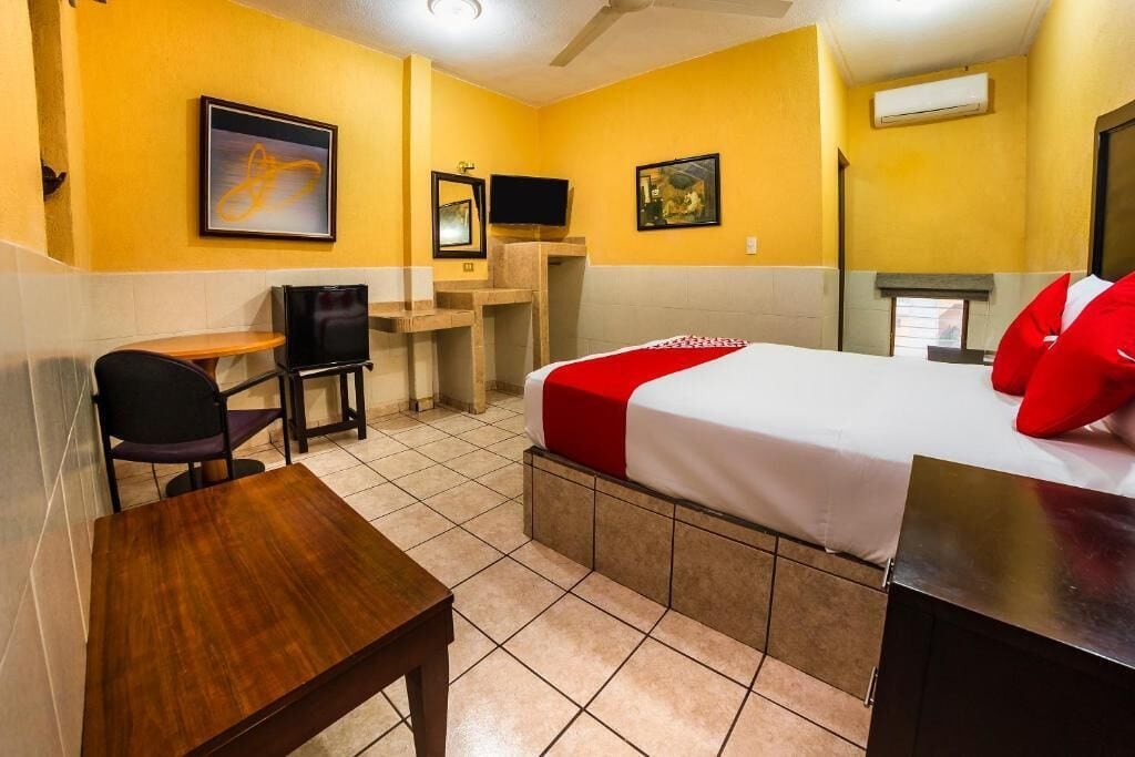 A hotel room with a bed, a desk, a chair, a television, and artwork on the walls.