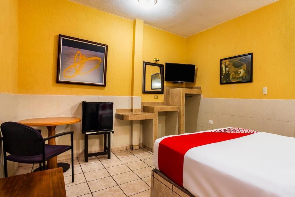 A hotel room with a bed, a desk, a chair, a television, and artwork on the walls.