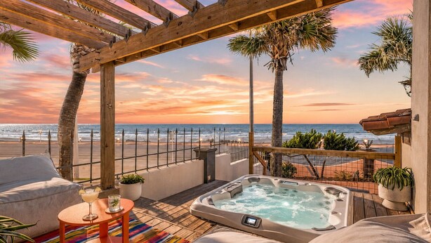 Eine Holzpergola mit Blick auf den Strand, einem Whirlpool und einer Lounge mit einem farbenfrohen Teppich.