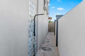 Un étroit couloir extérieur, avec un mur carrelé d’un côté et un chemin de béton menant à une porte.