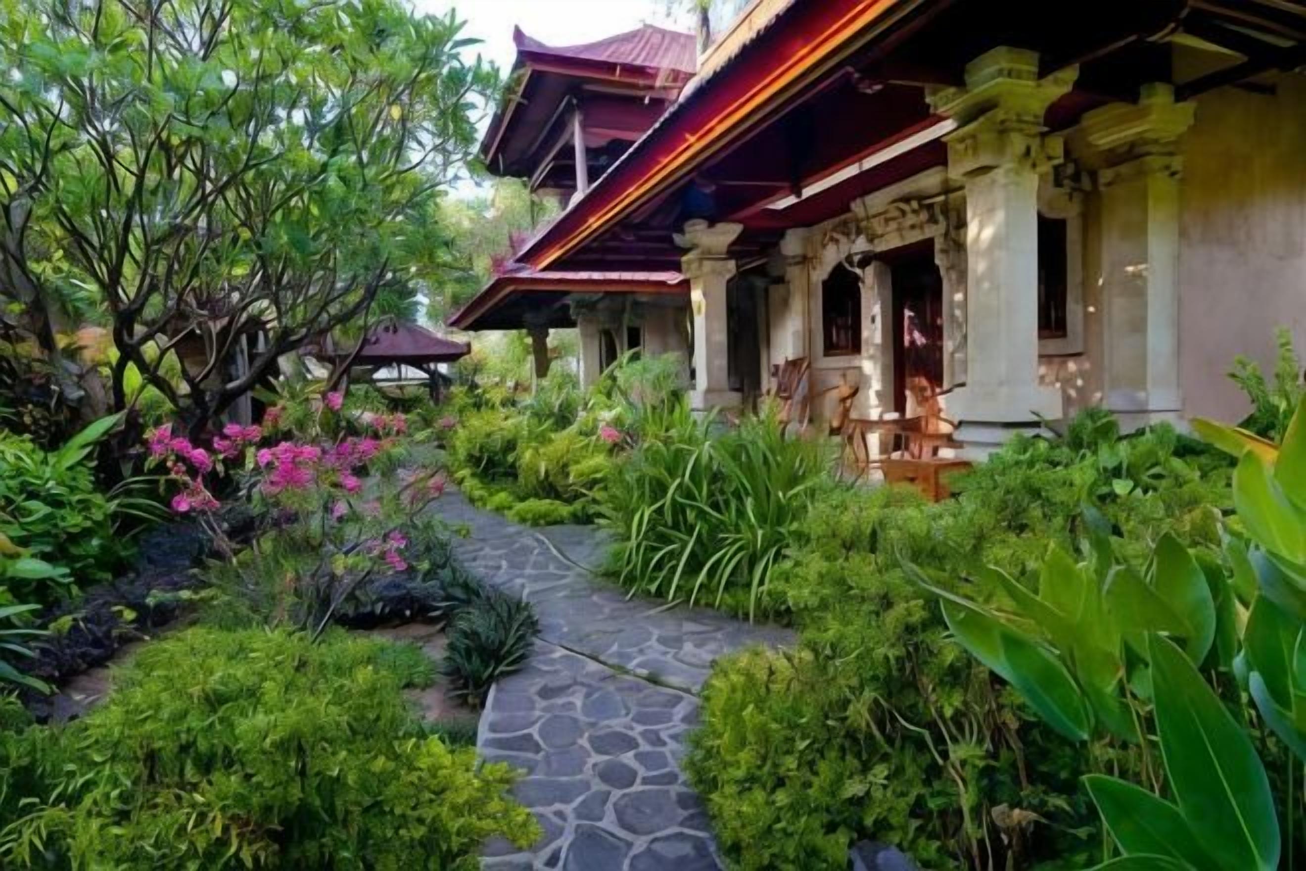 Un edificio tradicional con un camino de piedra que lleva a una entrada cubierta, rodeado de exuberante vegetación y plantas en flor.