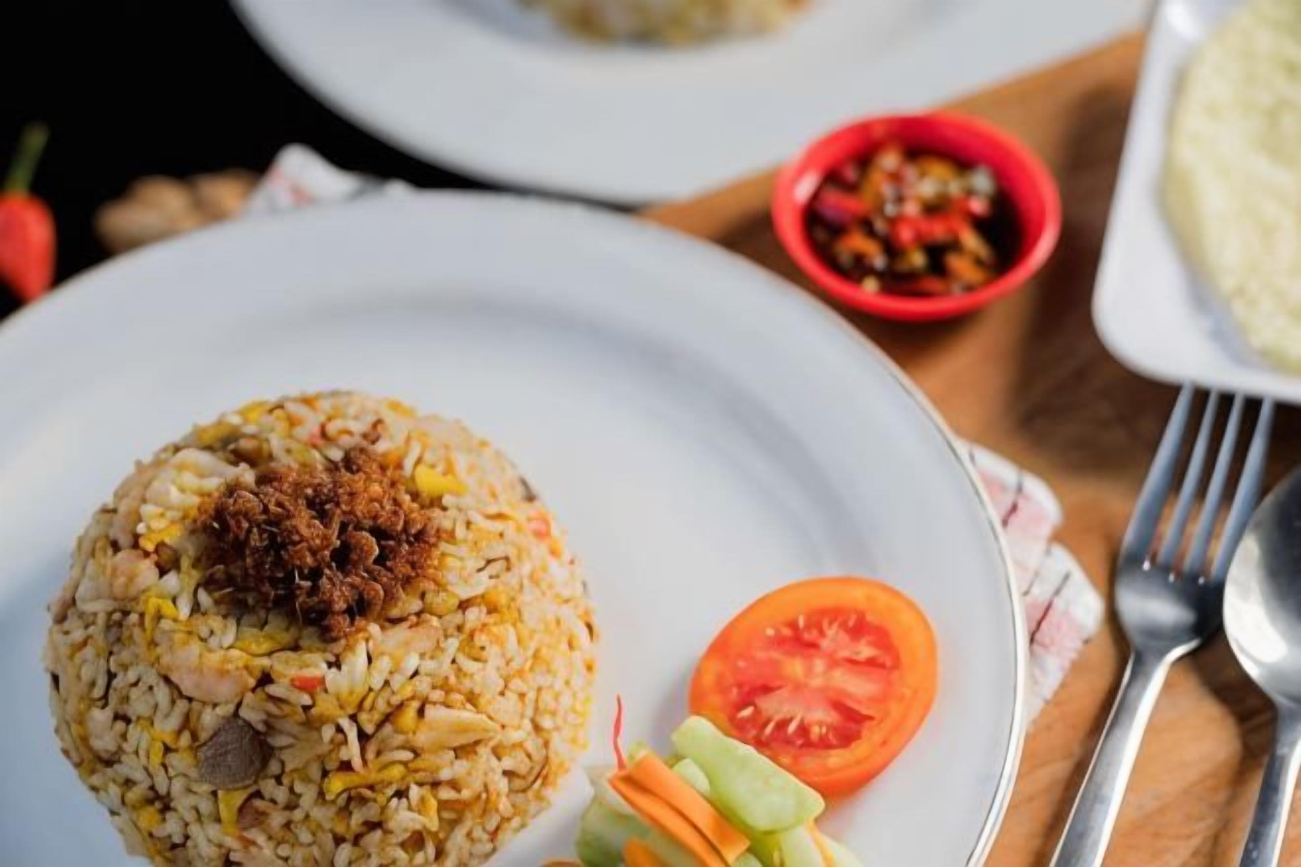 A plate of fried rice with a garnish on top, accompanied by a slice of tomato and some vegetables.