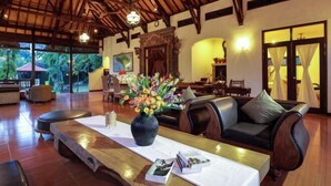 A spacious indoor area with a wooden ceiling, a dining table with chairs, a sofa, and a vase of flowers. - Banyualit Spa 'n Resort Lovina (Bali)