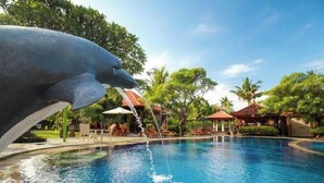 A swimming pool with a dolphin sculpture spouting water, surrounded by lounge chairs and umbrellas. - Banyualit Spa 'n Resort Lovina (Bali)
