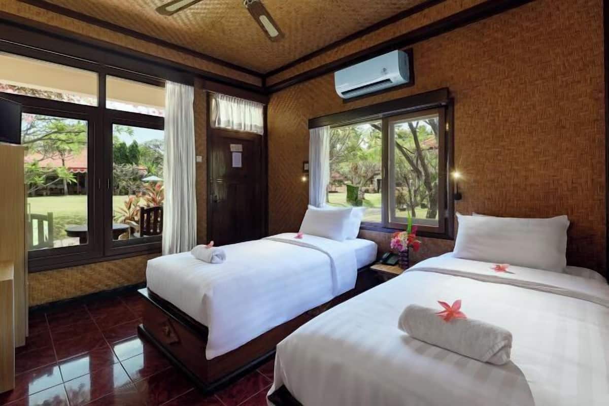 Habitación de hotel con dos camas, una ventana con vistas al jardín y un equipo de aire acondicionado en la pared.