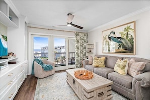A living room with a grey sofa, a wooden coffee table, a white cabinet, and a large window with a view of buildings.