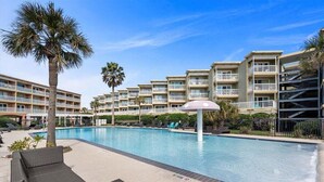 Ein Swimmingpool mit Liegestühlen und Palmen, umgeben von mehrstöckigen Gebäuden mit Balkonen.