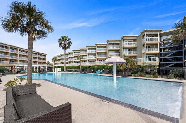 A swimming pool with lounge chairs and palm trees, surrounded by multi-story buildings with balconies.