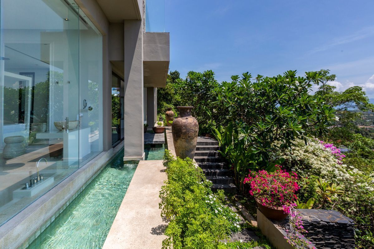 A modern outdoor pool area with clear water, surrounded by lush greenery and a stone staircase leading to a higher level.