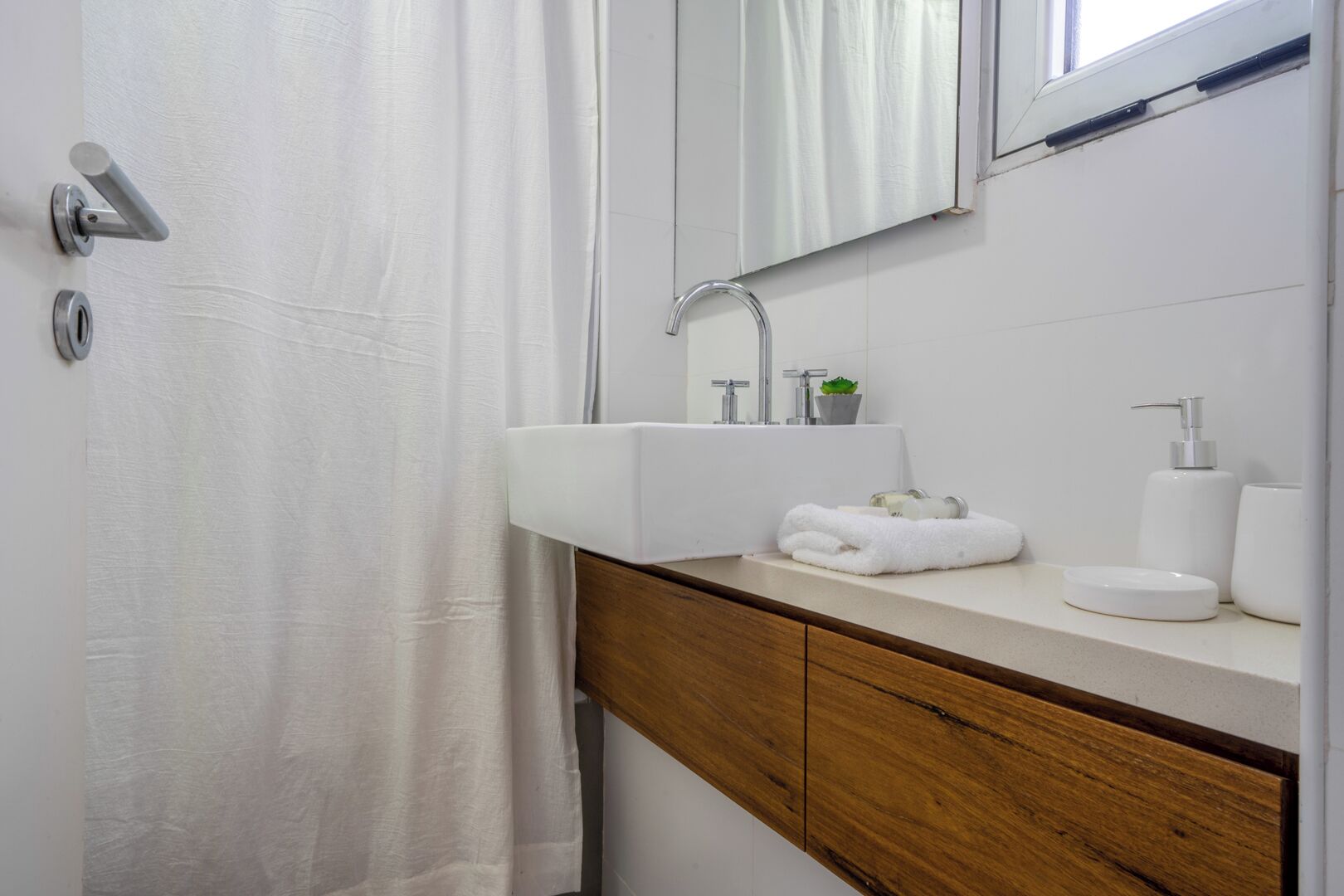 Un baño con lavamanos blanco, tocador de madera y cortina de ducha.