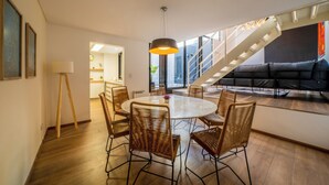 Un salon moderne avec une table à manger ronde, des chaises en osier, un canapé noir et un escalier menant à un niveau supérieur.