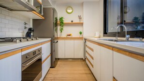 Une cuisine moderne avec des armoires blanches, des comptoirs en bois, une cuisinière en acier inoxydable, un four encastré, un réfrigérateur, un évier avec un robinet et une horloge au mur.