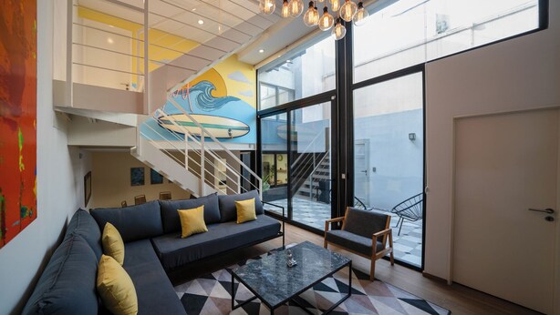 Un salon moderne avec un canapé noir, des coussins jaunes, une table basse et un escalier menant à un balcon.