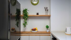 Une cuisine avec des étagères en bois, un saladier rempli de fruits, une plante en pot, une horloge et un panneau décoratif portant le mot « AMOUR ».