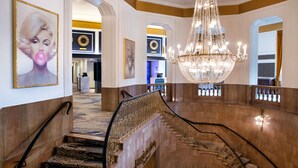 A grand staircase with a chandelier, marble walls, and framed artwork. - The Brock Niagara Falls Fallsview, Tapestry by Hilton (Niagara Falls)