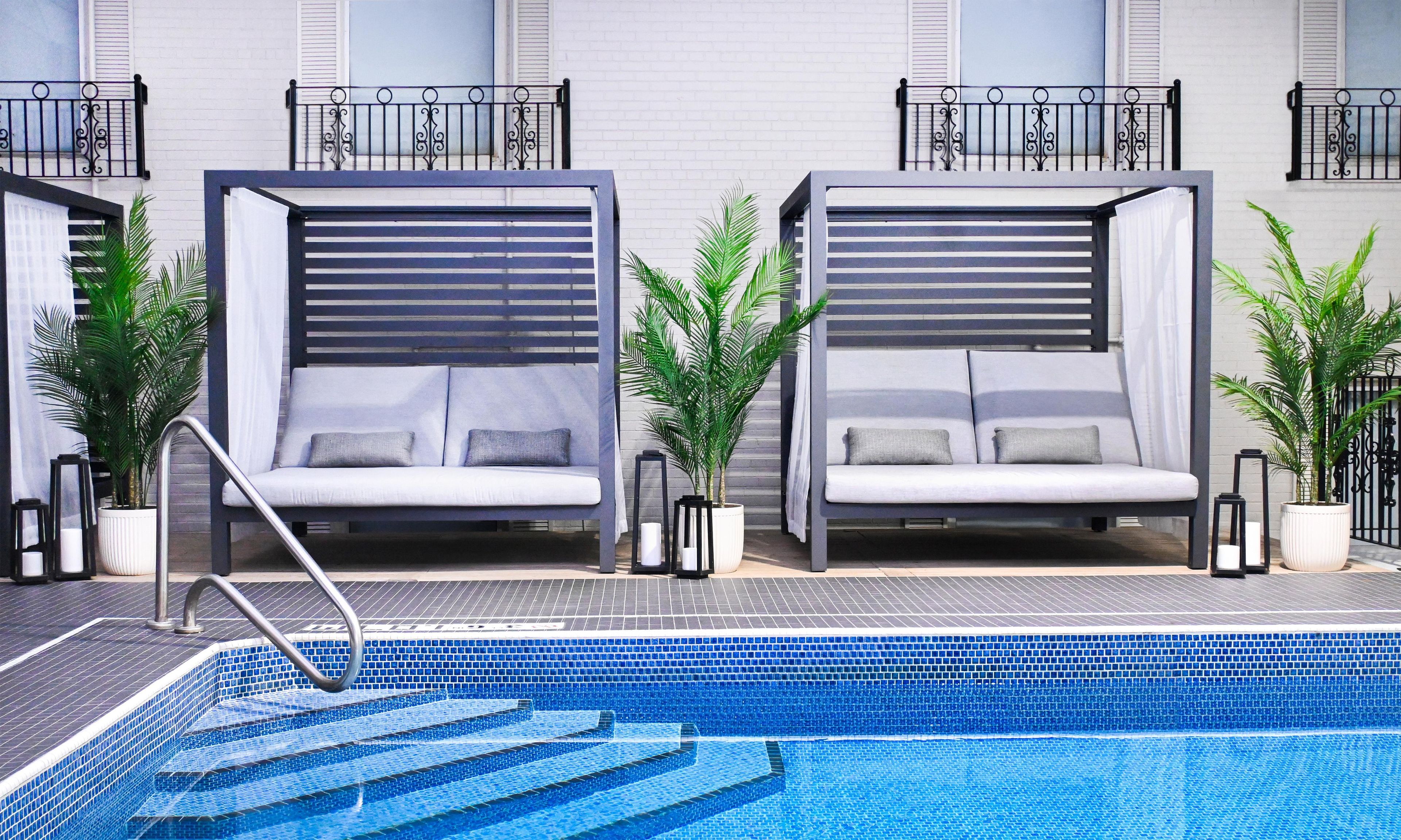 A modern hotel room with a pool, featuring two large beds with built-in headboards, a small pool area, and potted plants.