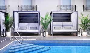 Una habitación de hotel moderna con piscina, que presenta dos camas grandes con cabeceros integrados, una zona de piscina pequeña y plantas en macetas.