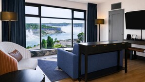 A hotel room with a large window offering a view of a waterfall and greenery. - The Brock Niagara Falls Fallsview, Tapestry by Hilton (Niagara Falls)