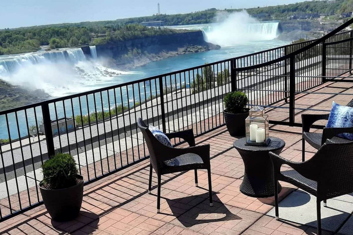 Un balcón con mobiliario exterior, con vistas a una cascada y un río.