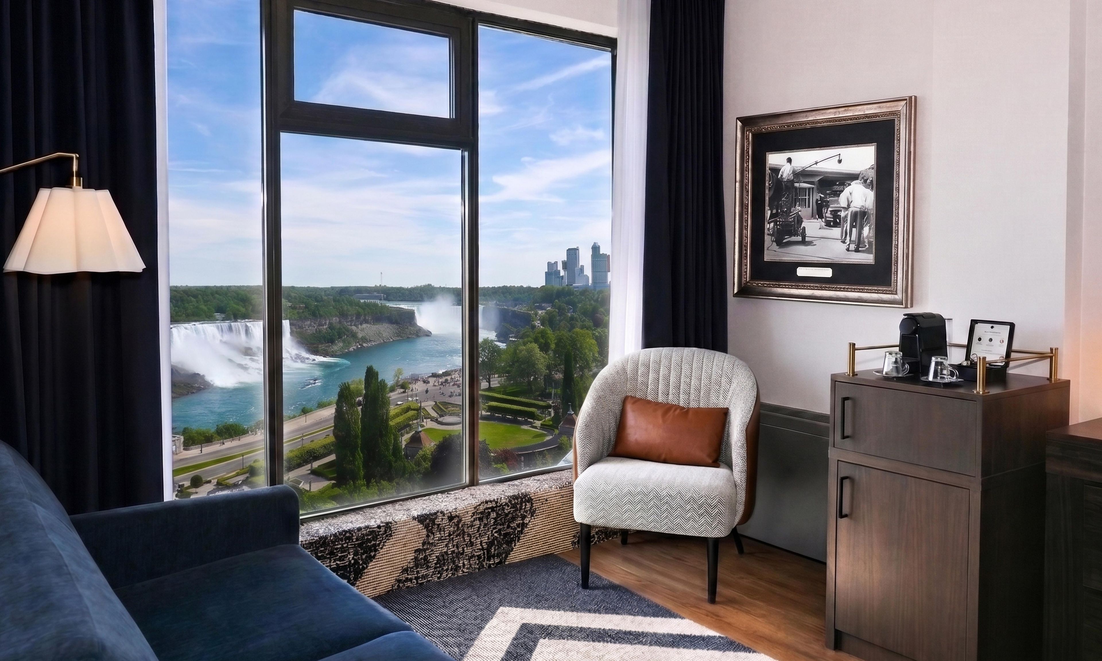 Habitación de hotel moderna con un ventanal que ofrece vistas a una cascada y al paisaje urbano.