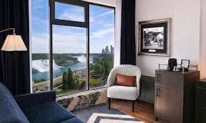 A modern hotel room with a large window offering a view of a waterfall and cityscape.