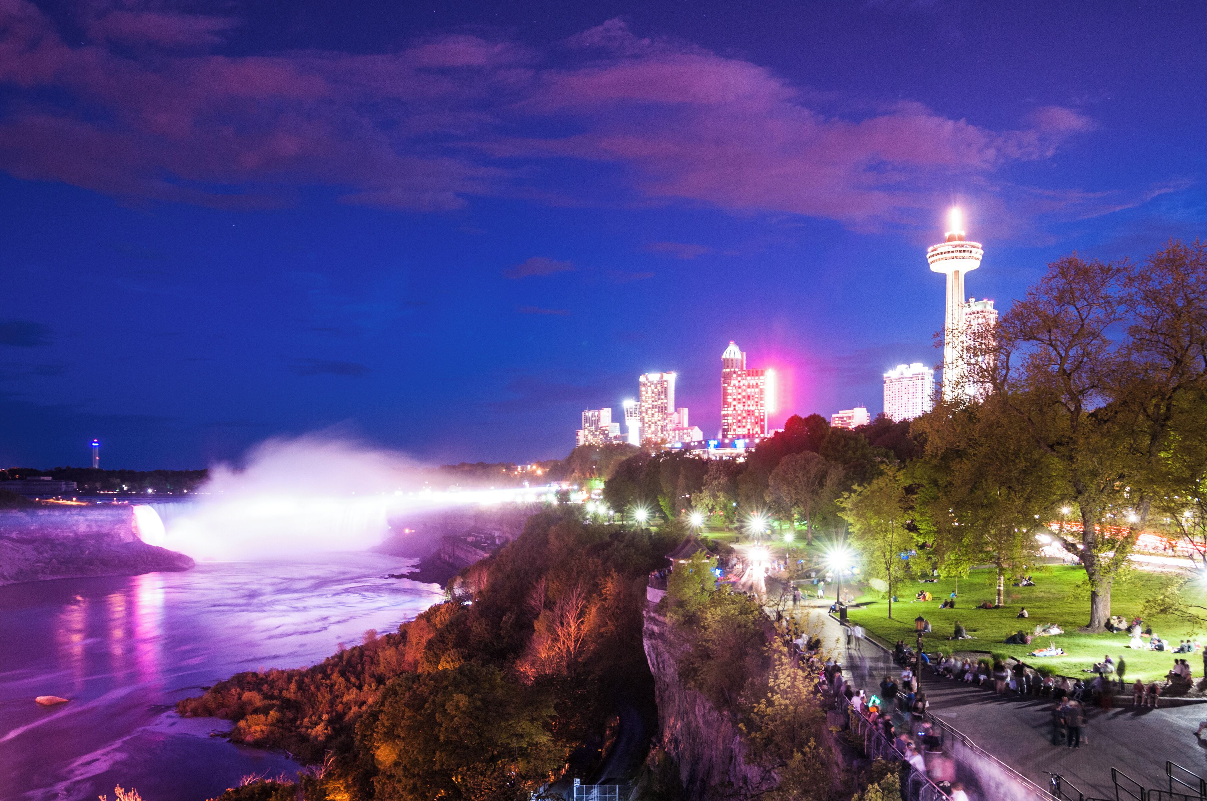A cityscape with a prominent tower, a waterfall, and a park area with people.