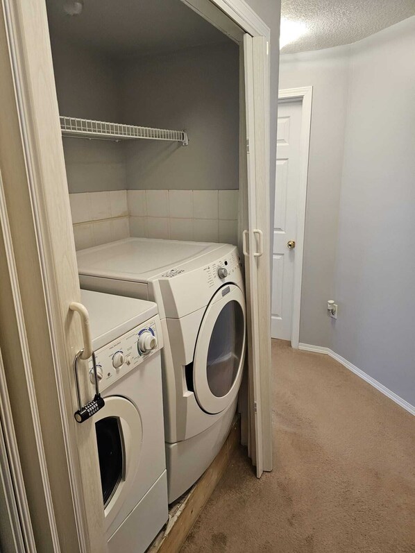 A laundry room with a front-loading washer and dryer, a tiled backsplash, and a door leading to another room.