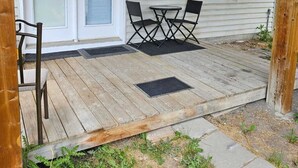 A covered porch with a wooden deck, a sliding glass door, and a small table with chairs.