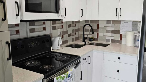 A modern kitchen with white cabinets, a microwave, a stove, and a sink.