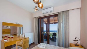 Hotelkamer met een bed, een bureau met een stoel, een spiegel, een radiator, een airconditioning en een balkon met uitzicht op zee, plus een tafel met een lamp.