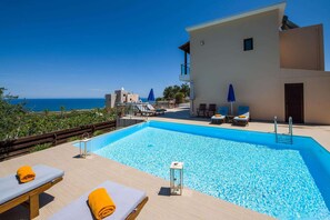 Relax by the pool with a clear view of the sea, surrounded by lounge chairs and a glass-enclosed seating area.