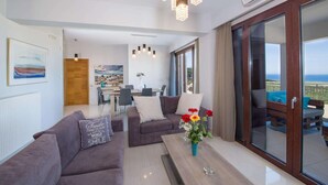 Een moderne woonkamer met een bank, een bijzettafeltje met bloemen en uitzicht op zee door grote schuifdeuren.