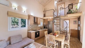 A spacious living area with a sofa, a dining table with chairs, a kitchen with a refrigerator, and a spiral staircase. - Rigilis - Two Bedroom Villa, Sleeps 4 (Nydri)
