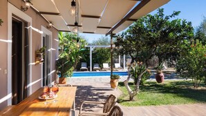 A patio with a wooden table and wicker chairs, a pool in the background, and potted plants around. - Rigilis - Two Bedroom Villa, Sleeps 4 (Nydri)