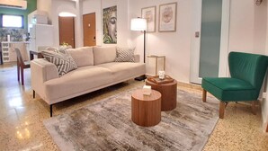 A modern living room with a sofa, a green armchair, and a coffee table. There is a kitchen area in the background.