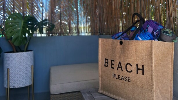 A beach-themed tote bag with the text "BEACH PLEASE" on a wooden bench.