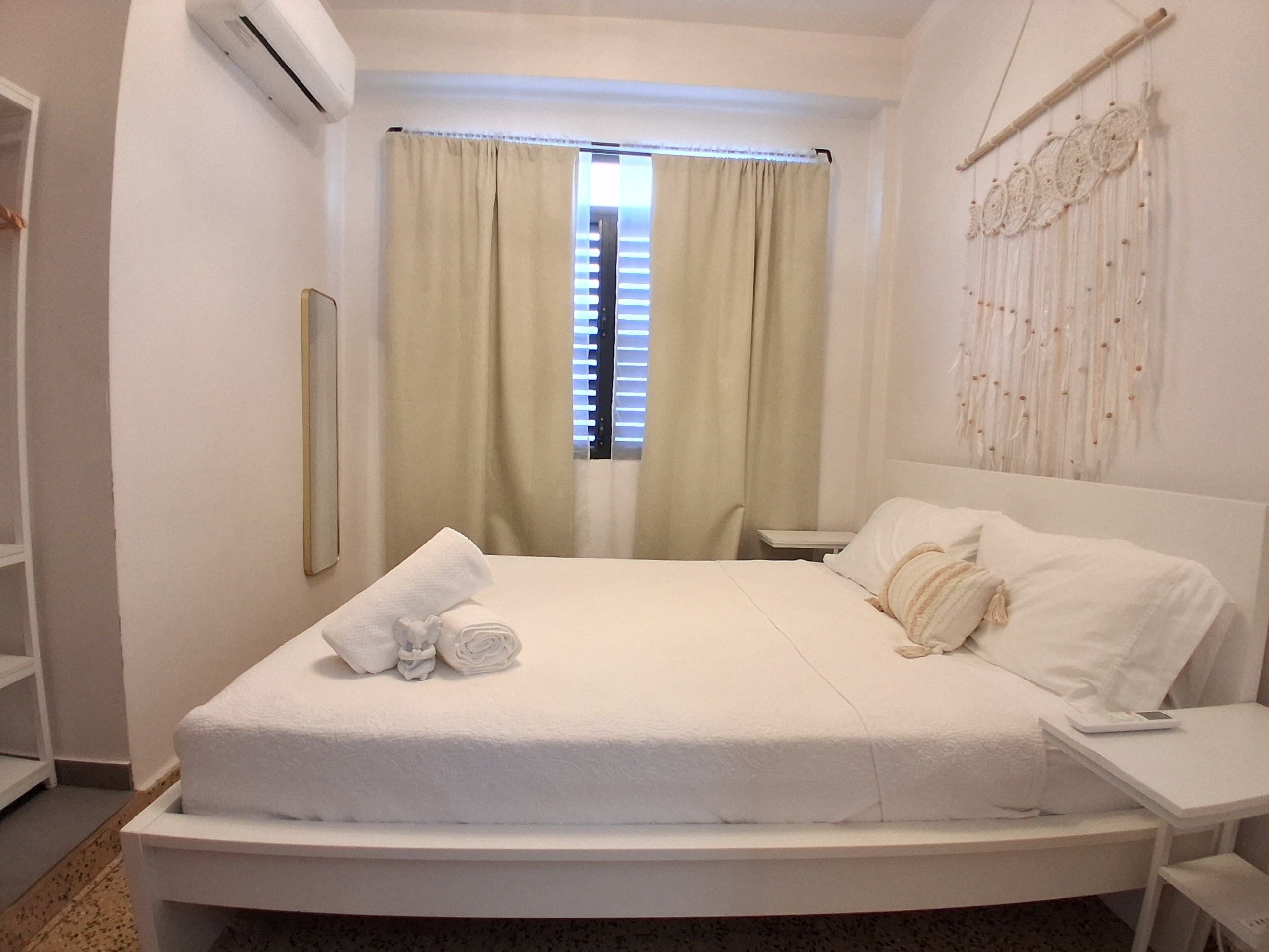 Un lit bien fait, avec une couette blanche et des oreillers, une table de chevet avec une lampe et un climatiseur fixé au mur.