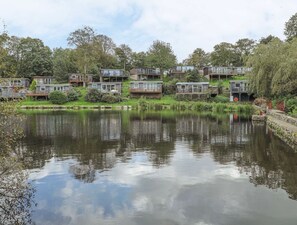 Uma série de cabanas modernas com varandas, localizadas à beira de um lago tranquilo, cercadas por vegetação exuberante.