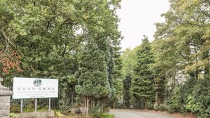 Schild für den Glangwna Country Holiday Park, mit einer gewundenen Straße, die durch einen bewaldeten Bereich führt.